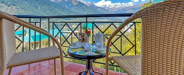 A balcony with wicker chairs, a table with a vase and teacups, and a mountain view.