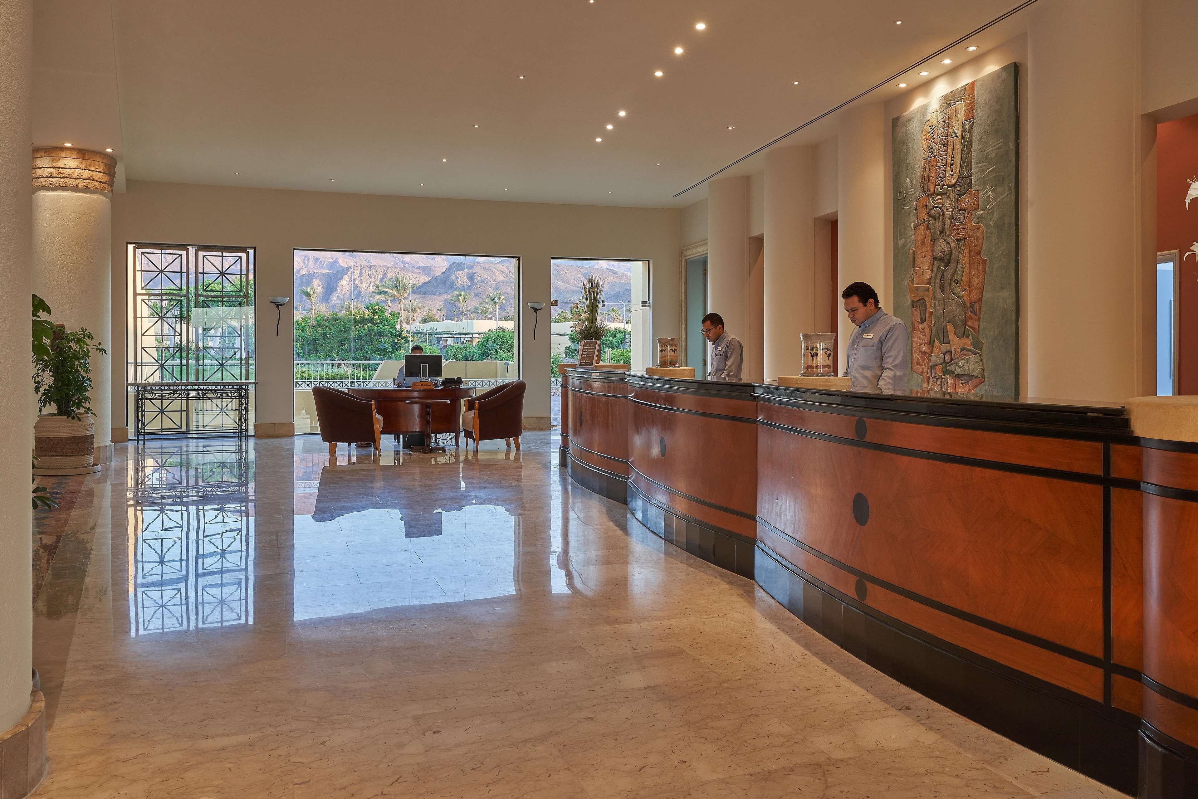 A hotel reception area with a polished marble floor, a reception desk, and a large window offering a view of the mountains.