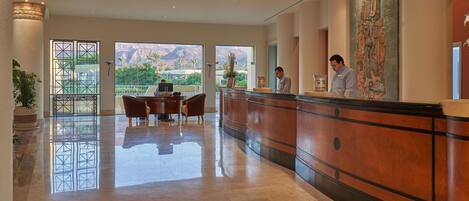A hotel reception area with a polished marble floor, a reception desk, and a large window offering a view of the mountains.