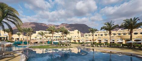 A resort pool with palm trees, a clear sky, and mountains in the background.