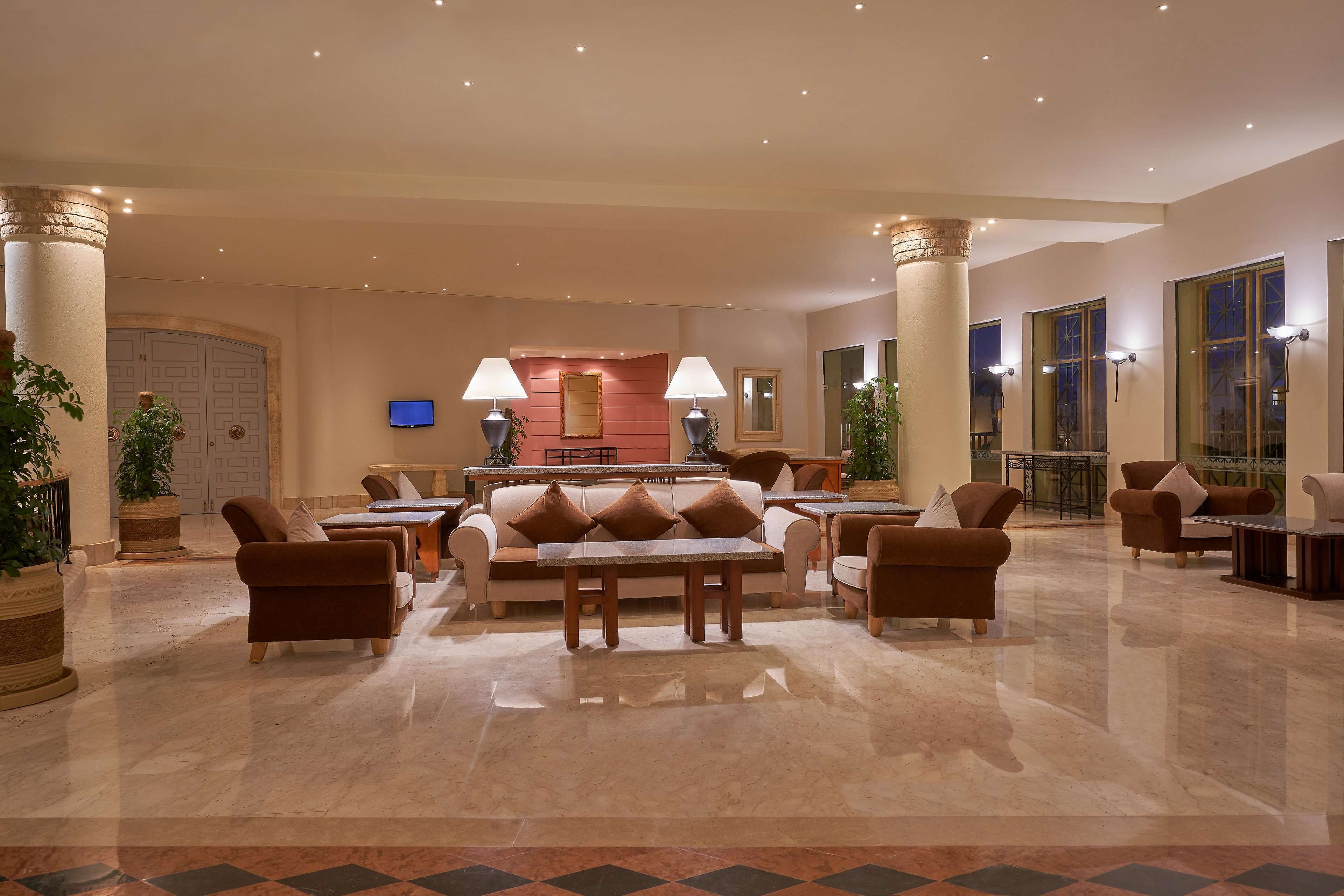 A spacious lobby with a central seating area, a television mounted on the wall, and a reception desk in the background.