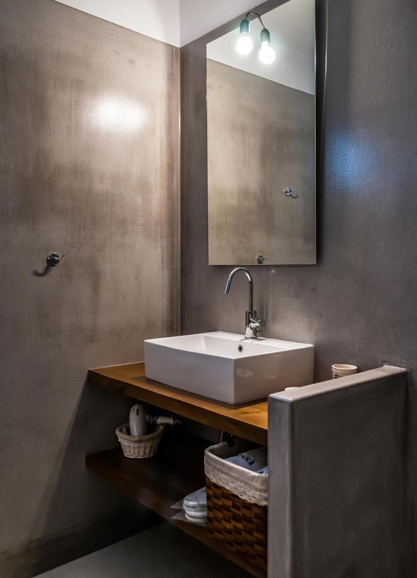 Un baño moderno con un lavamanos rectangular, un espejo con dos luces y un estante de madera con cestas.