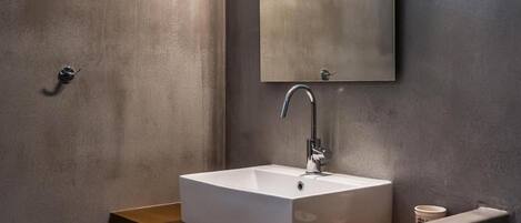 Un baño moderno con un lavamanos rectangular, un espejo con dos luces y un estante de madera con cestas.