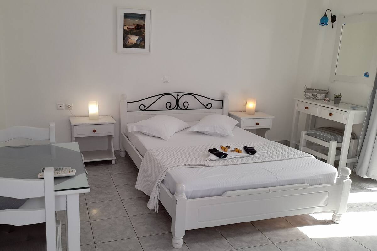 Quarto branco com cama, mesas de cabeceira, escrivaninha e uma cadeira.