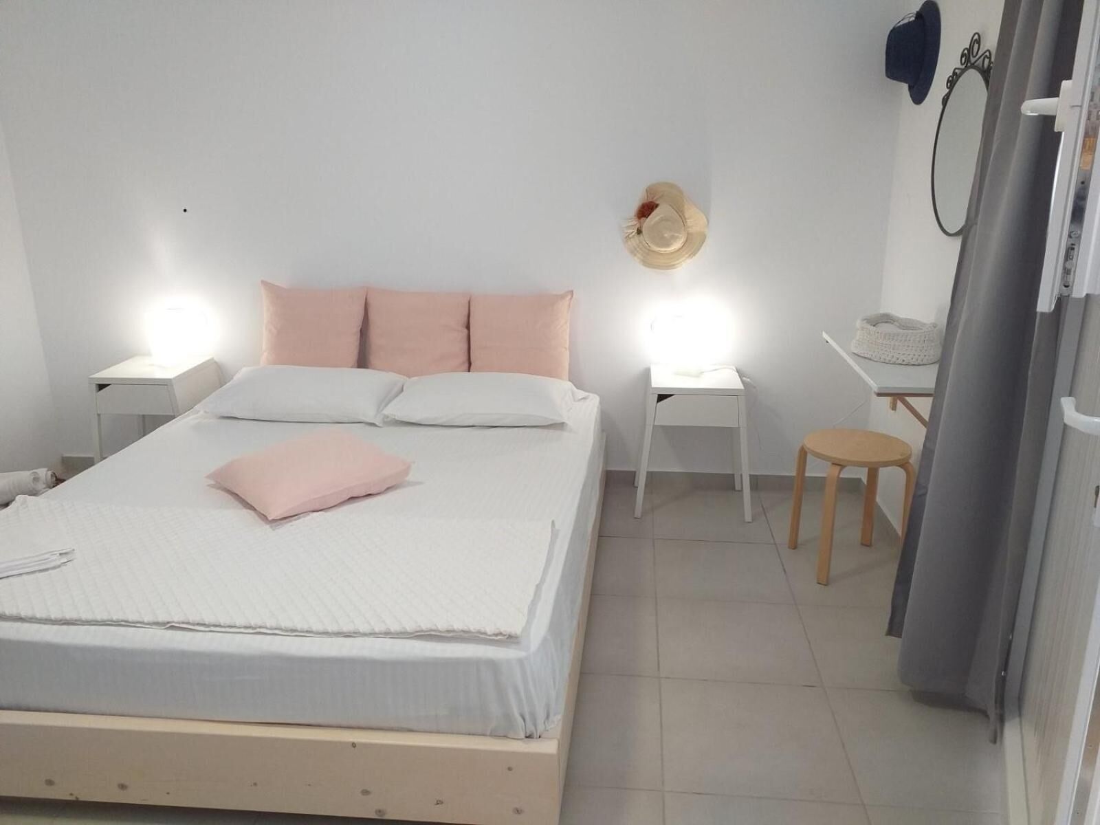 A bedroom with a bed, two bedside tables, a small stool, a wall-mounted hat, and a curtain.