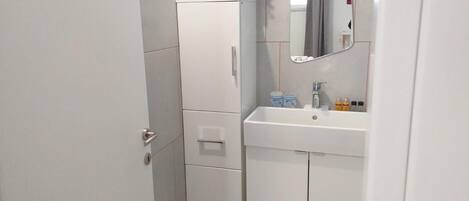 A bathroom with a white sink, mirror, and cabinets. There is a plant on the sink and toiletries on the counter.