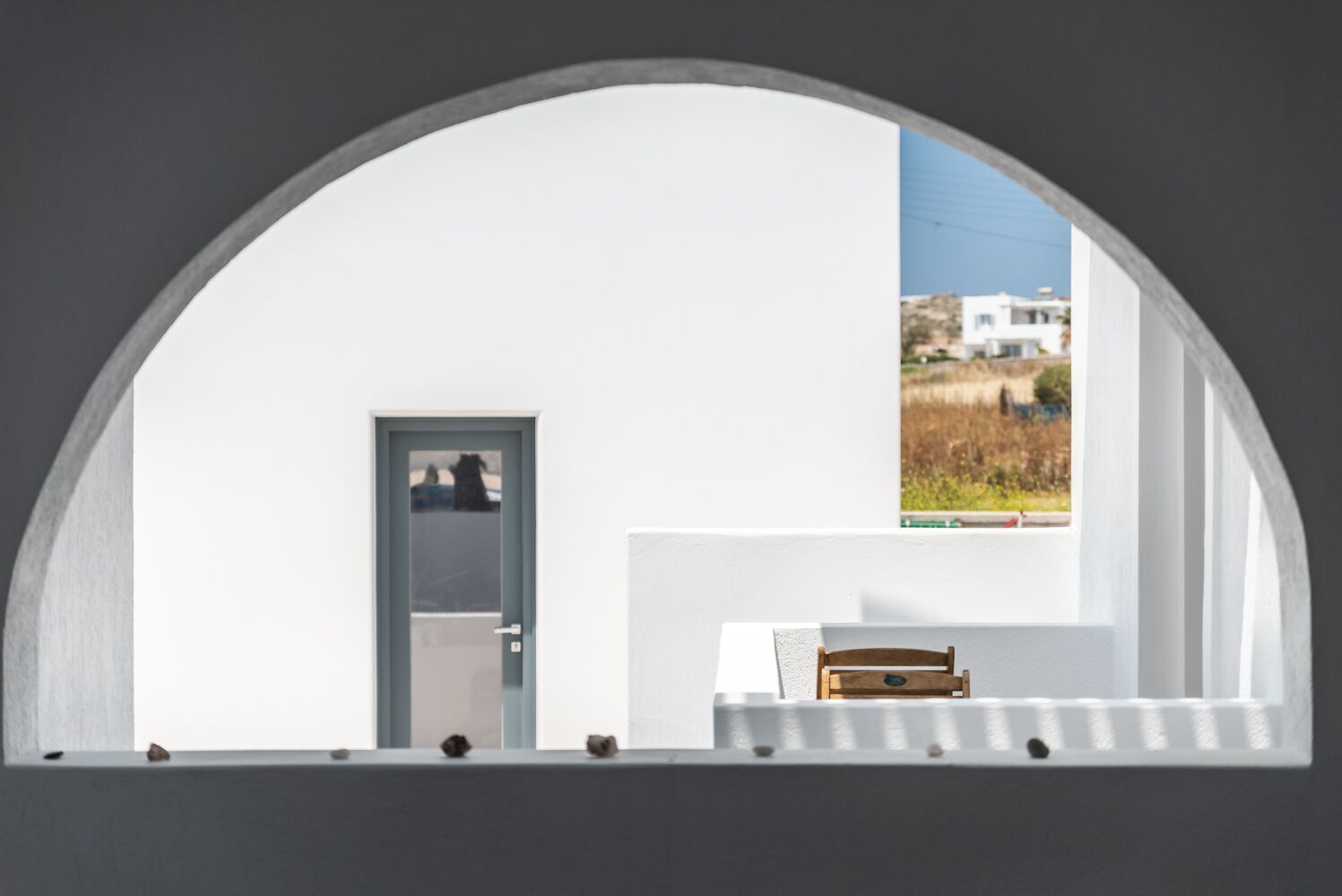 Una habitación con pared blanca, una puerta y una ventana que da a una casa y un campo.