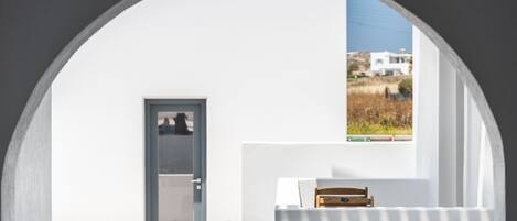 Una habitación con pared blanca, una puerta y una ventana que da a una casa y un campo.