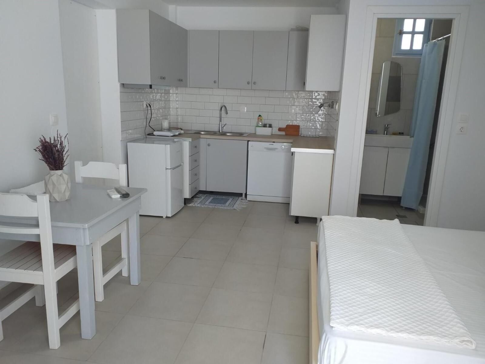 A compact kitchen with white cabinets, a small refrigerator, a sink, and a dishwasher.