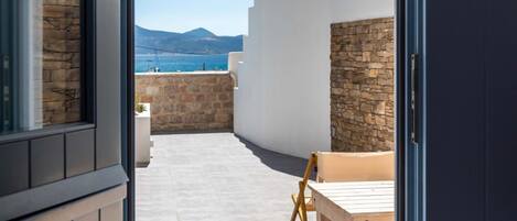 Puerta abierta que da a un patio con mesa y sillas, un muro de piedra y vistas al mar y a las montañas.