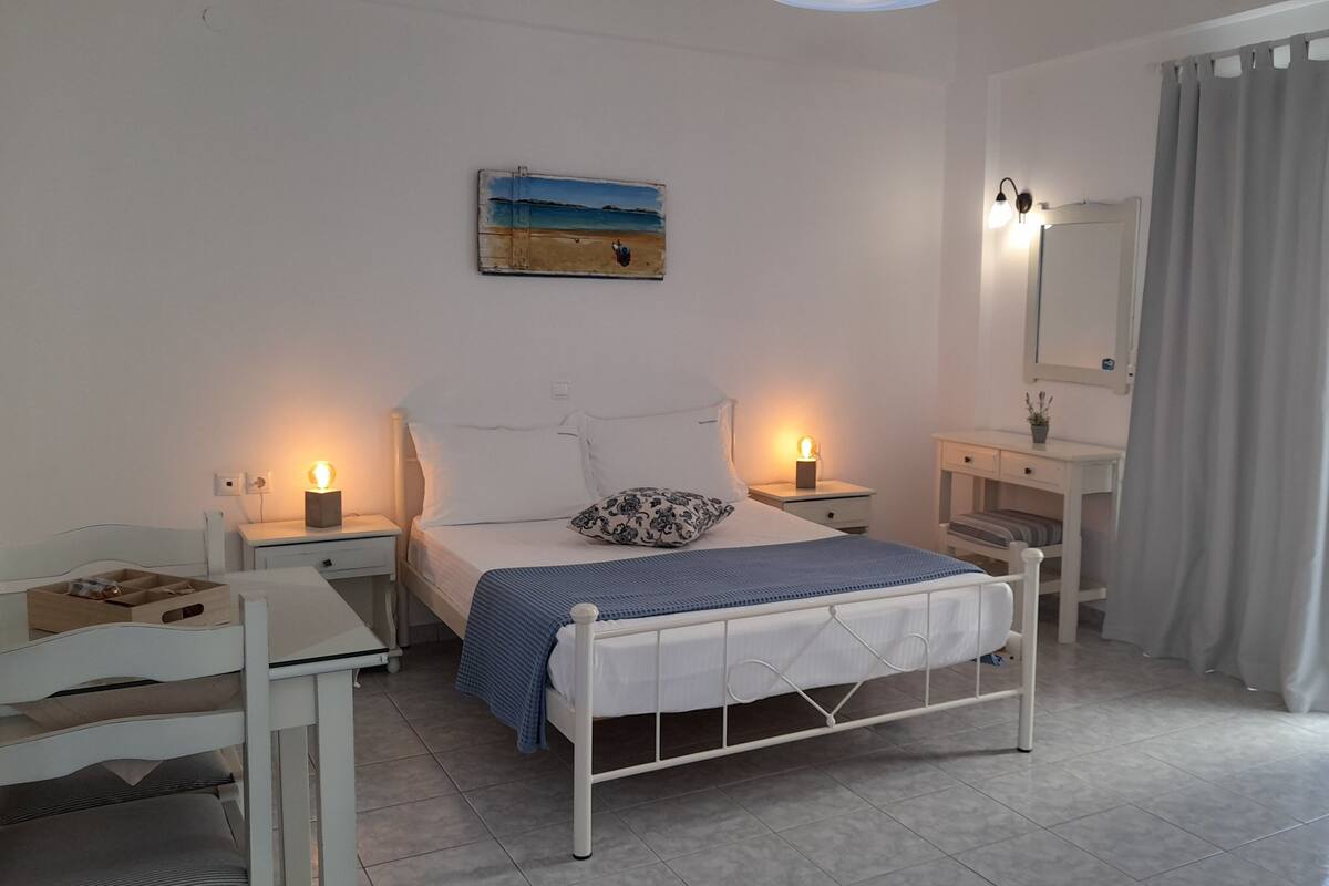 Quarto com cama, mesas de cabeceira, penteadeira, espelho e vista para o exterior.