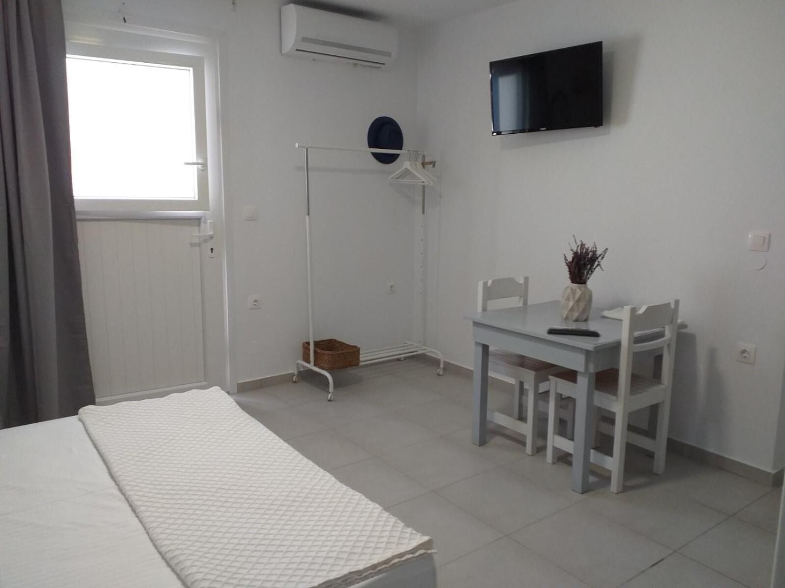 A room with a bed, a desk with chairs, a television, and a window.