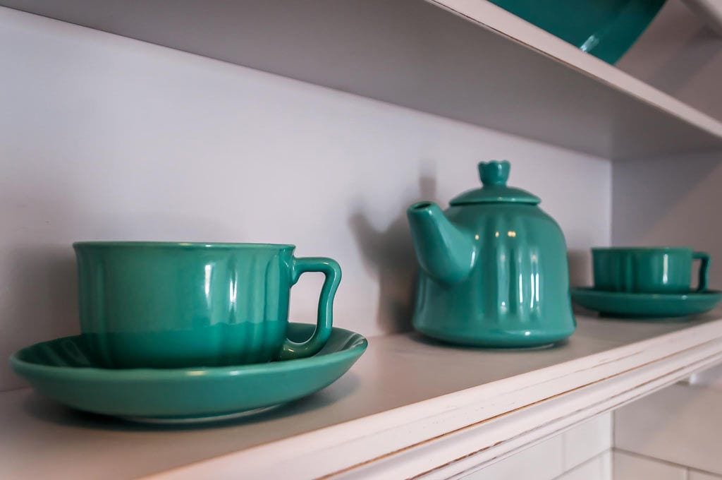 Una tetera azul turquesa y tazas a juego sobre una estantería blanca.