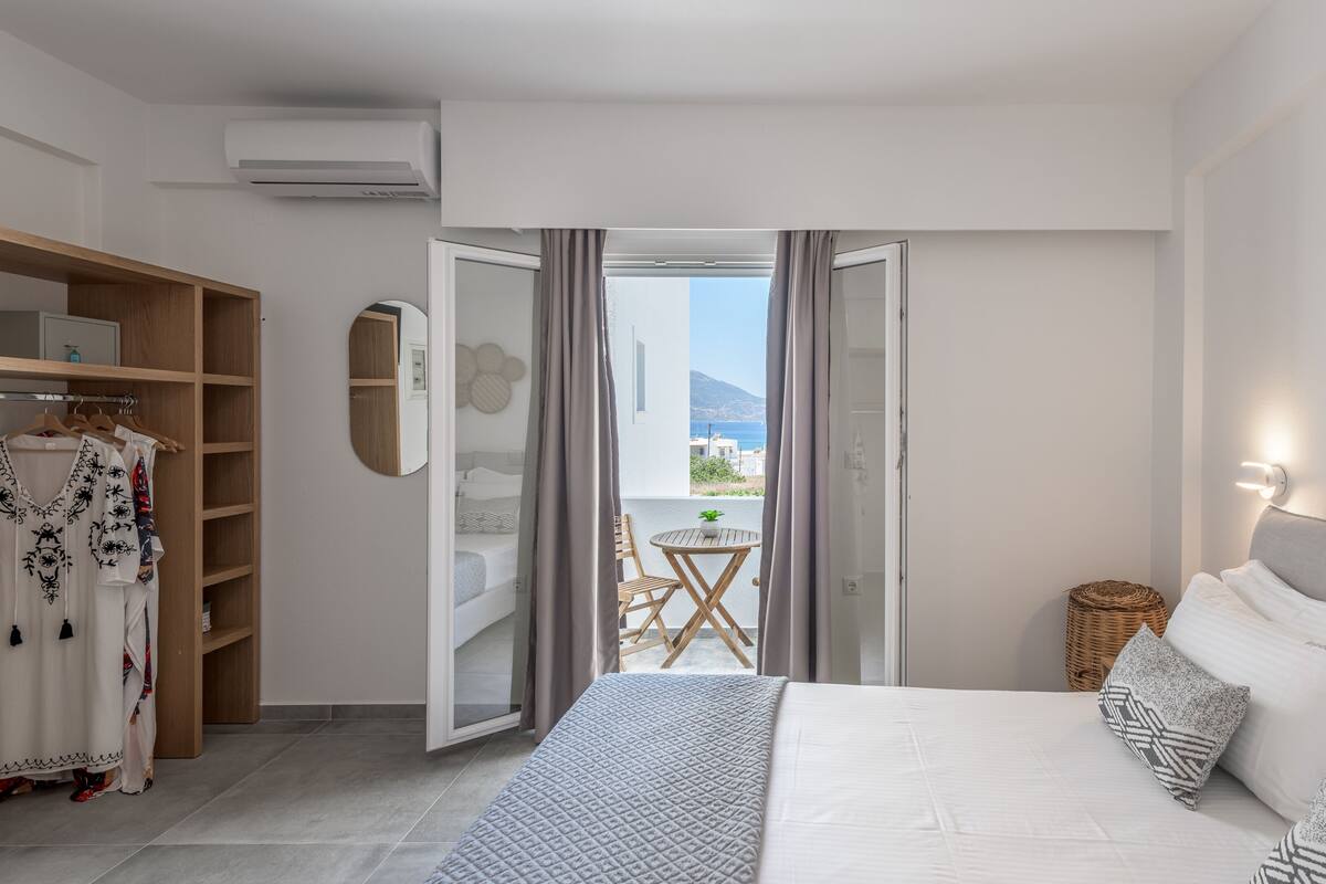 Quarto com cama, guarda-roupa, banheiro e varanda com vista para o mar.