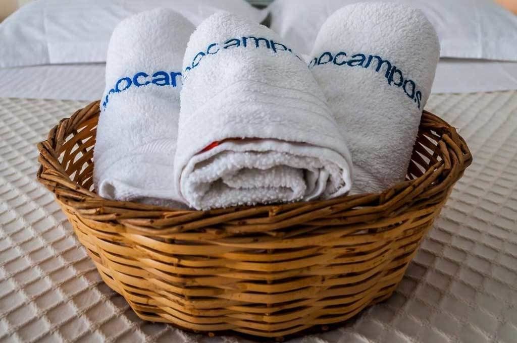 A wicker basket containing three white towels with "ocampob" embroidered on them, placed on a textured surface.