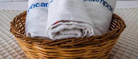 A wicker basket containing three white towels with "ocampob" embroidered on them, placed on a textured surface.