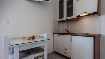 Une cuisine compacte avec des meubles blancs, une table à plateau en verre et un four encastré.