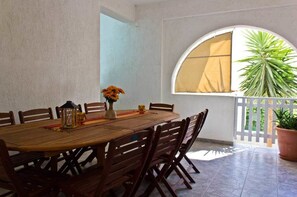 A dining area with a round wooden table, six chairs, a vase with flowers, a lantern, and a window with a view of greenery. - Ippocampos (Milos)