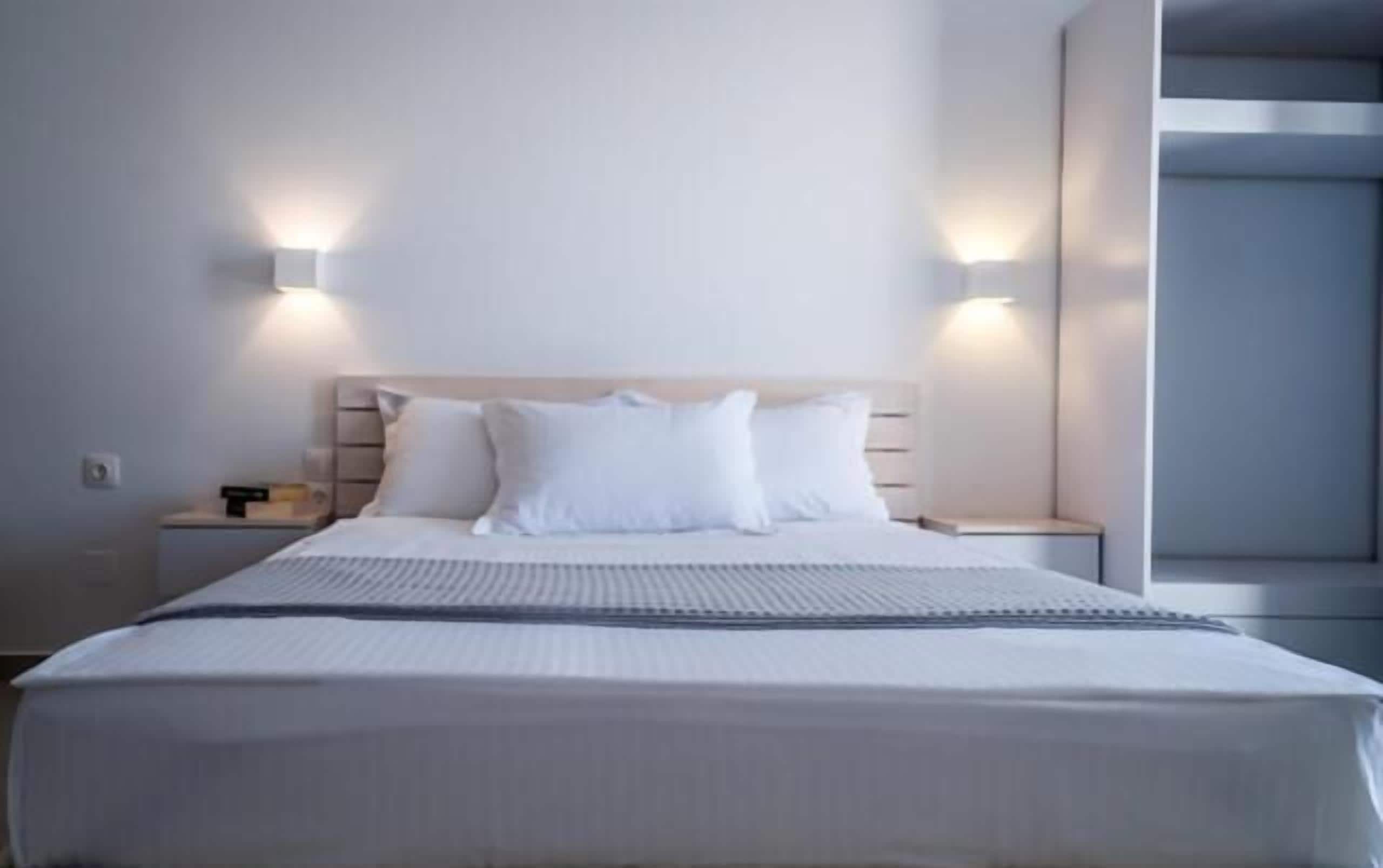 Quarto de hotel moderno com uma cama grande, duas mesas de cabeceira e iluminação embutida na parede.