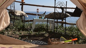 A tent with a view of the sea, a metal chair, and a table with a cushion.