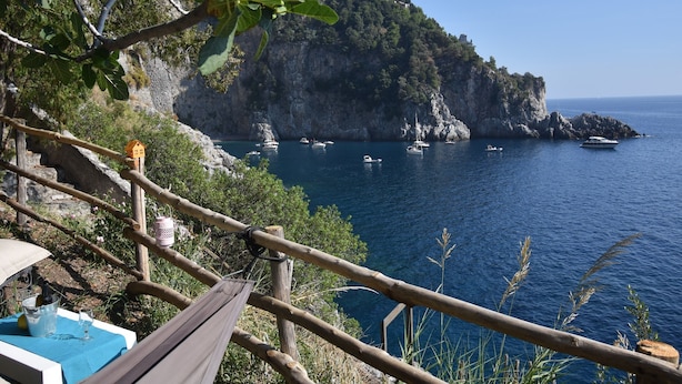 A coastal view with a wooden deck overlooking the sea, a table with a blue tablecloth, and a building on a cliff.