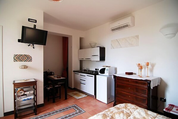 Una habitación pequeña con cama, kitchenette, televisión y escritorio.