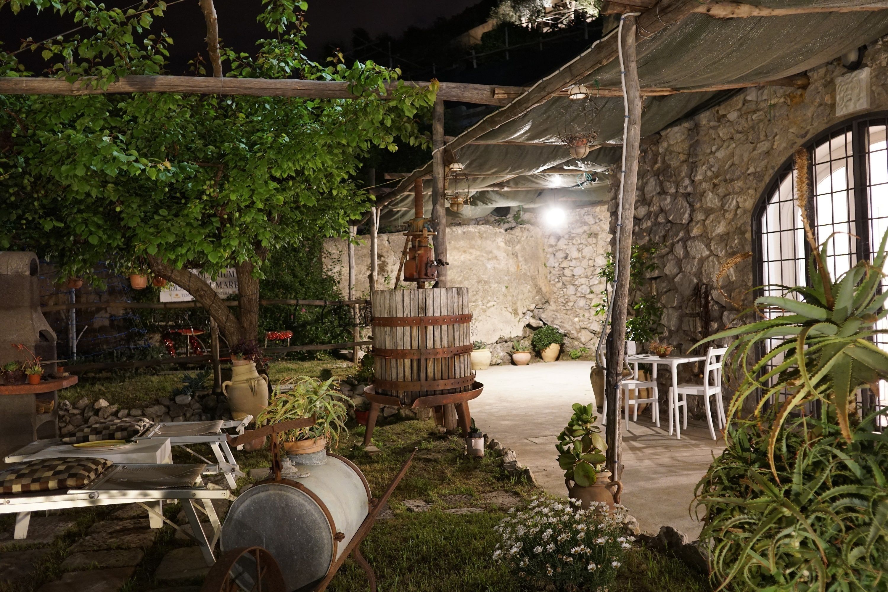 An outdoor patio with stone walls, wooden furniture, and potted plants.