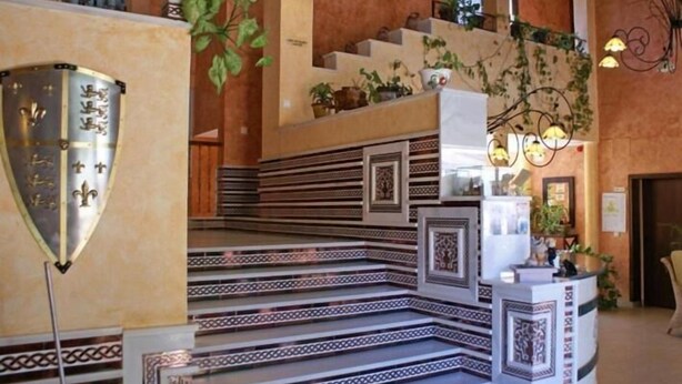 Un magnifique escalier orné de motifs complexes, menant à un palier où se trouvent un comptoir d’accueil et des plantes en pot.