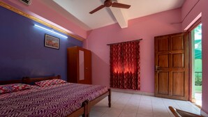 A bedroom with a bed, a ceiling fan, a door, and a window with curtains. - Nelmar Nest Guest House (Calangute)