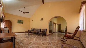 A spacious living area with a high ceiling, a ceiling fan, a patterned floor, and a wooden door. - Nelmar Nest Guest House (Calangute)