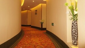 Ein Hotelkorridor mit Teppichboden, einer mit Blumen bepflanzten Vase rechts und einem Schild an der Wand.