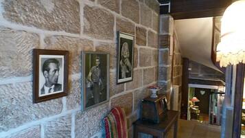 Un mur de pierre orné de portraits encadrés, un banc et une table avec un vase.