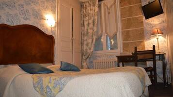 Une chambre à coucher avec un lit, un bureau, une chaise, un téléviseur et une fenêtre avec des rideaux.