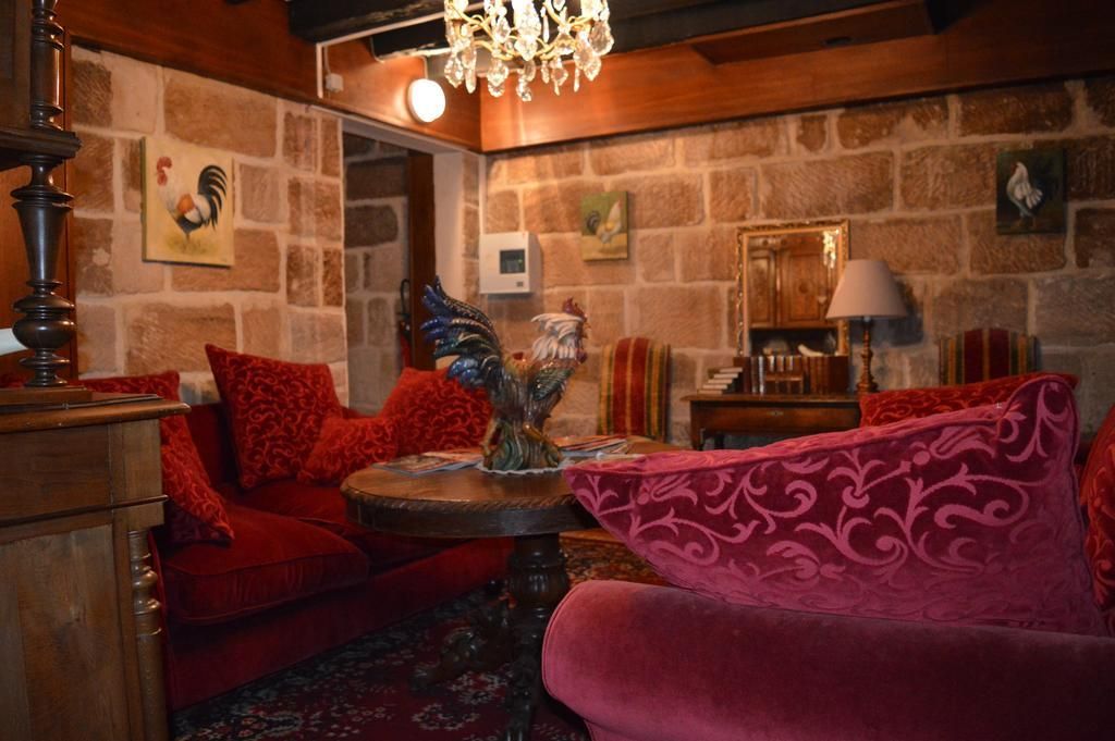 Une pièce chaleureuse avec un mur en pierre, un lustre, un canapé rouge, un fauteuil rose et un meuble en bois.