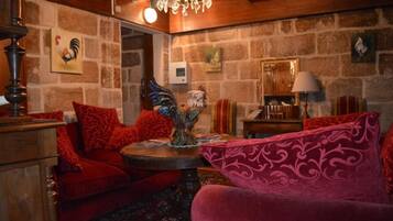 Une pièce chaleureuse avec un mur en pierre, un lustre, un canapé rouge, un fauteuil rose et un meuble en bois.