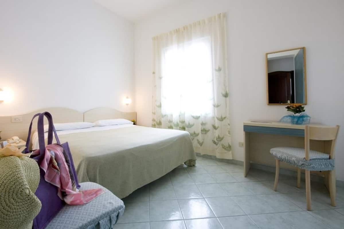Un dormitorio con cama, mesita de noche, silla y escritorio con espejo.