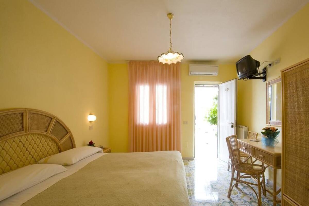Habitación de hotel con cama, escritorio, silla, televisor y ventana con cortinas.