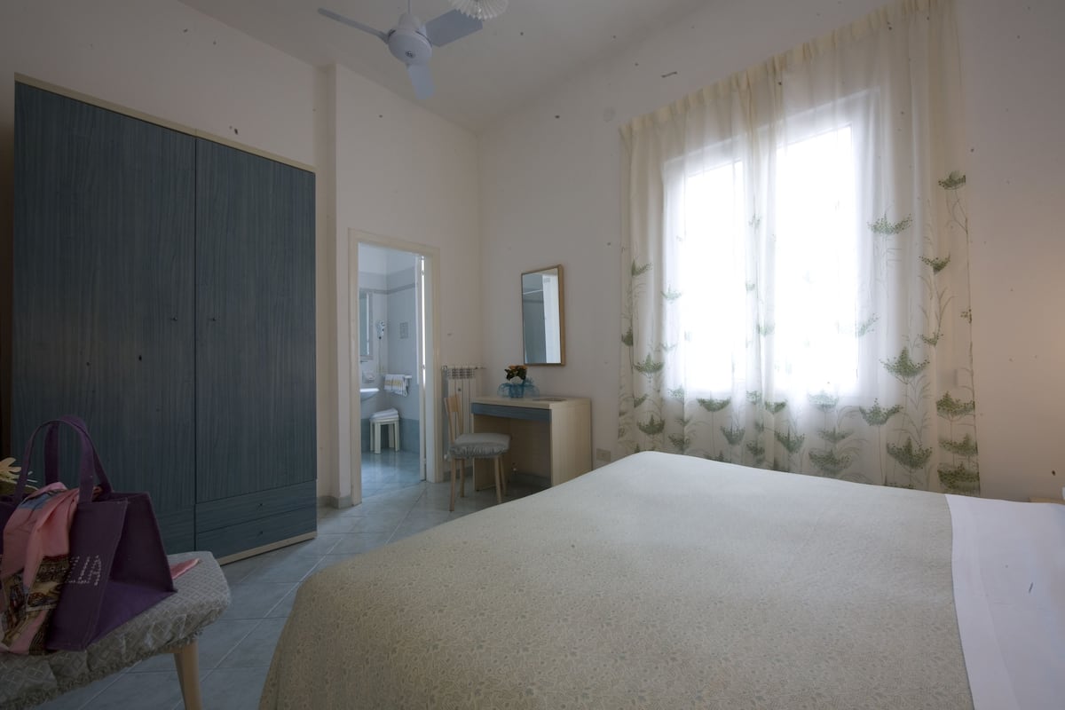 Un dormitorio con una cama, un escritorio, una silla, un armario, un espejo y una ventana con cortinas.