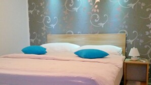 A bed with a wooden headboard and two pillows, a bedside table with a lamp, and a floral wallpaper pattern on the wall. - House Josipa (Plitvicka jezera)