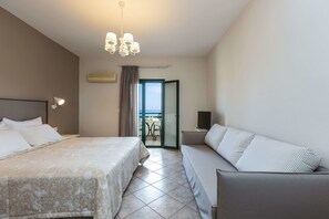 Quarto de hotel com cama, sofá, televisão e varanda com mesa e cadeiras.