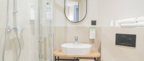 A modern bathroom with a glass shower enclosure, a white sink with a wooden countertop, a mirror, and a towel rack.