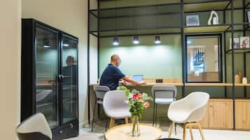 Un intérieur moderne où l’on voit un homme travaillant à un bureau, entouré de chaises et d’une petite table sur laquelle est posé un vase de fleurs.