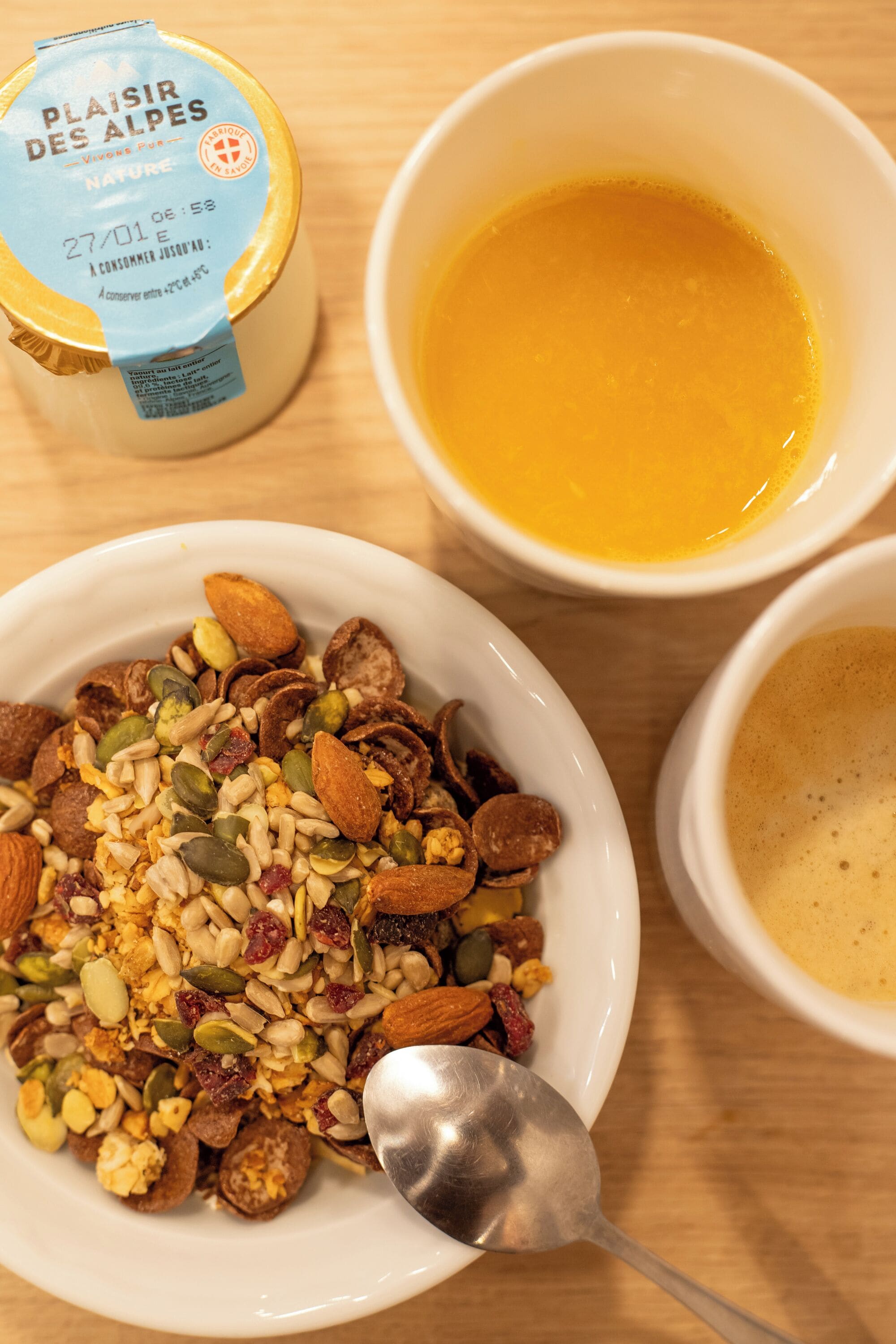 A breakfast setting with a bowl of granola, a jar of yogurt, and two cups of coffee.