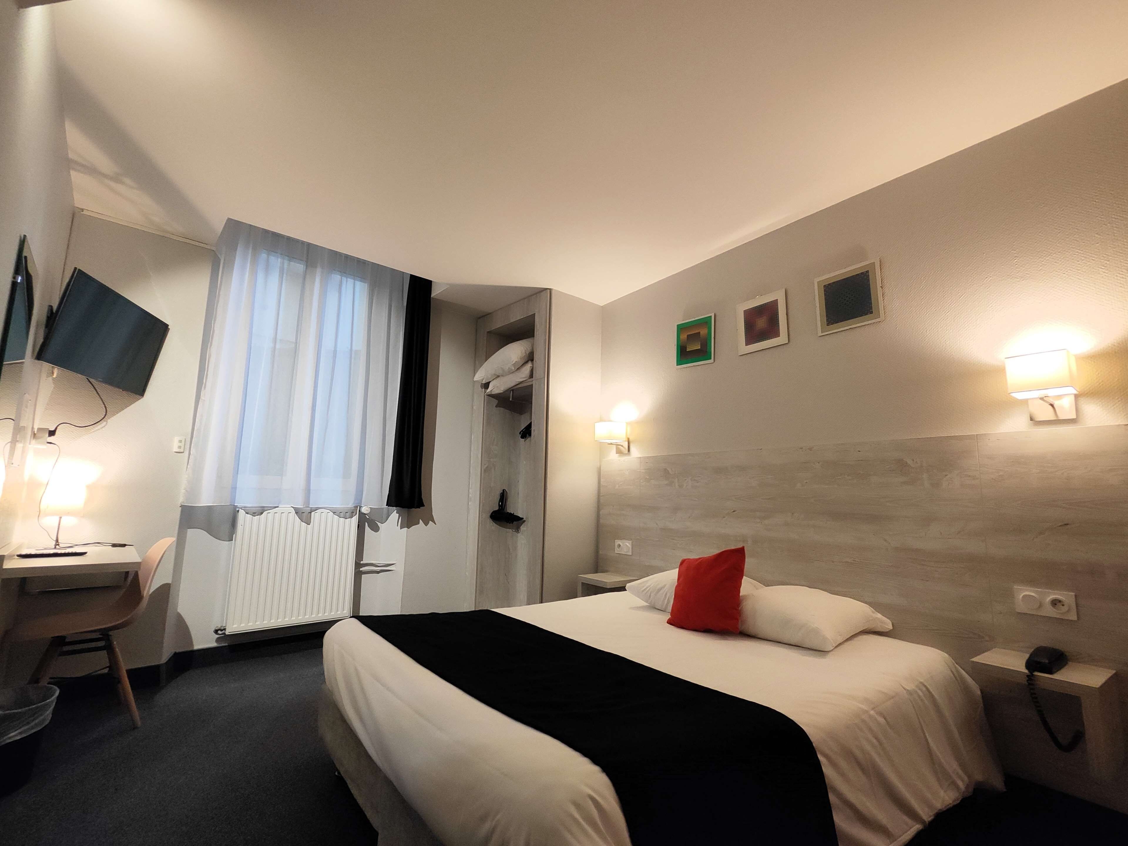 A hotel room with a bed, a desk, a chair, a TV, and a window with curtains.