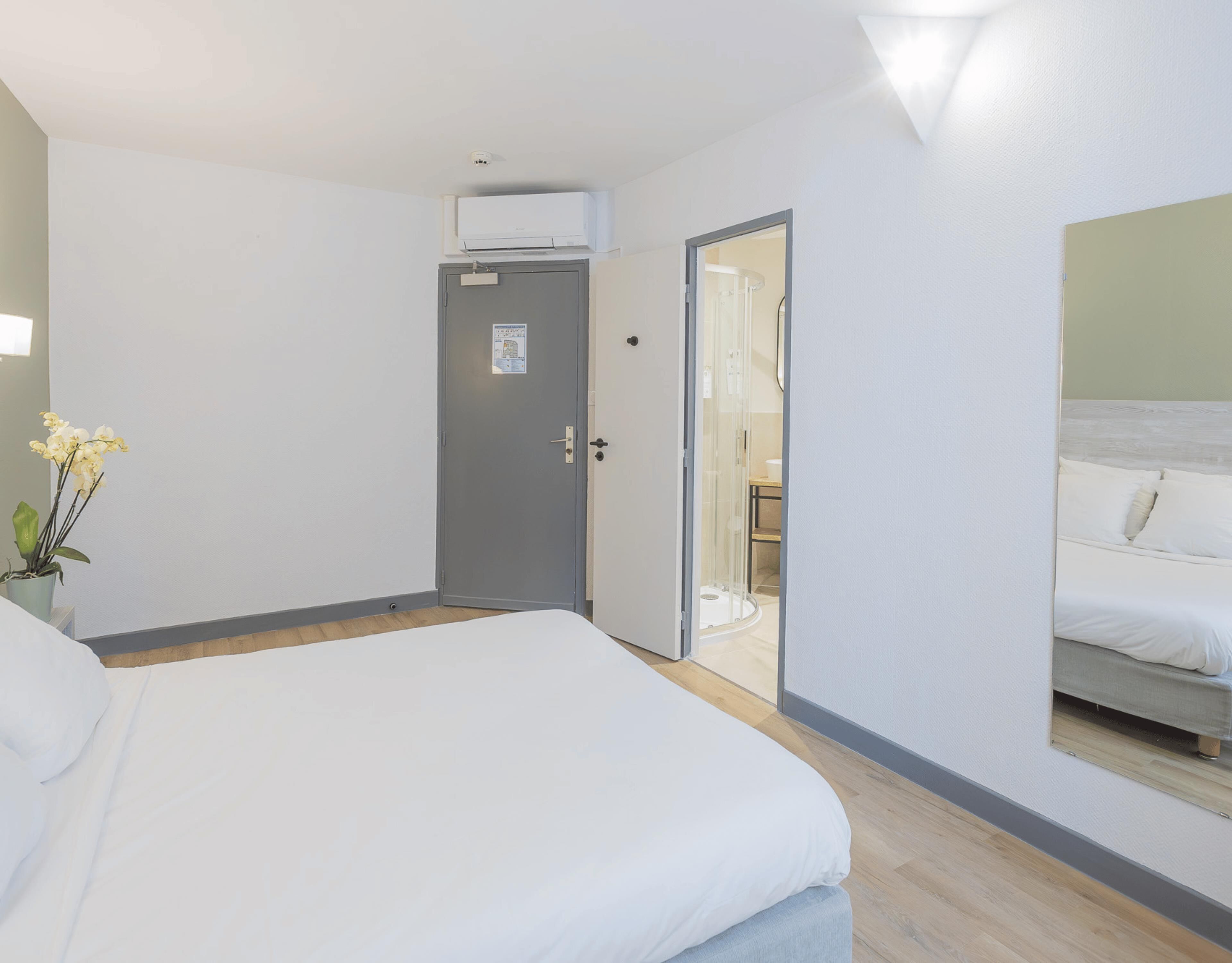 A hotel room with a bed, a door leading to a bathroom, and a shower area.