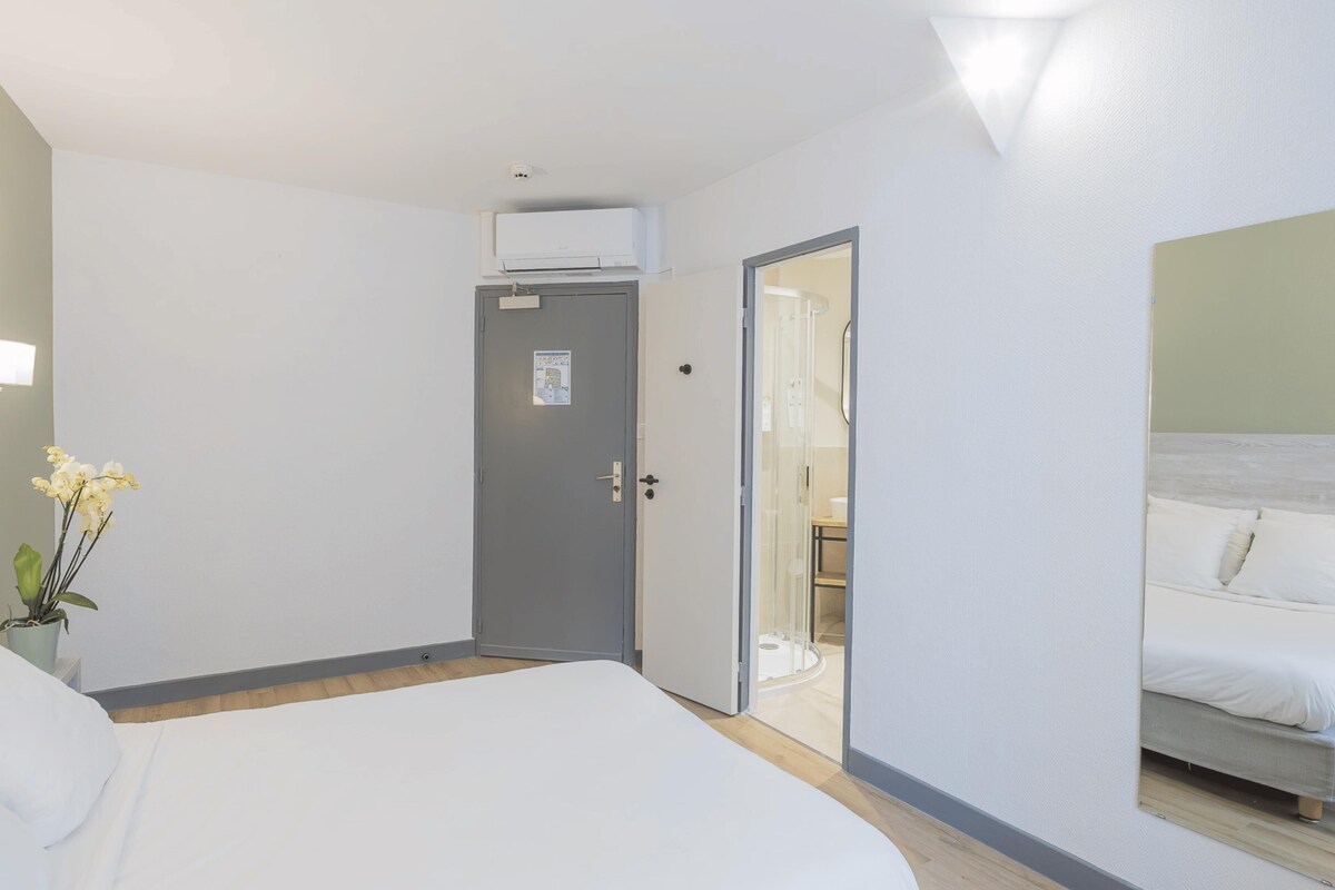 Habitación de hotel con cama, puerta que da a un baño y zona de ducha.