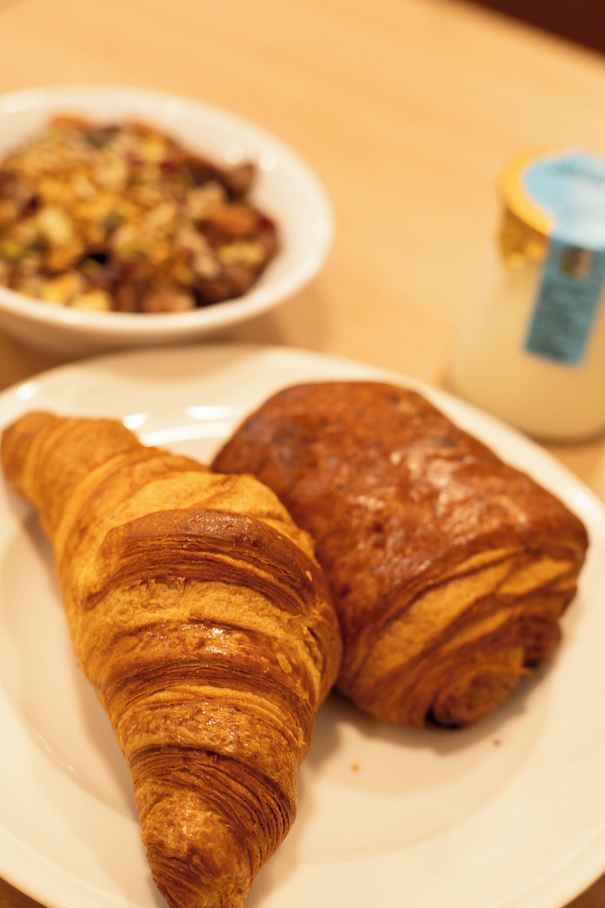 Un plato con dos croissants y un tazón pequeño de comida.