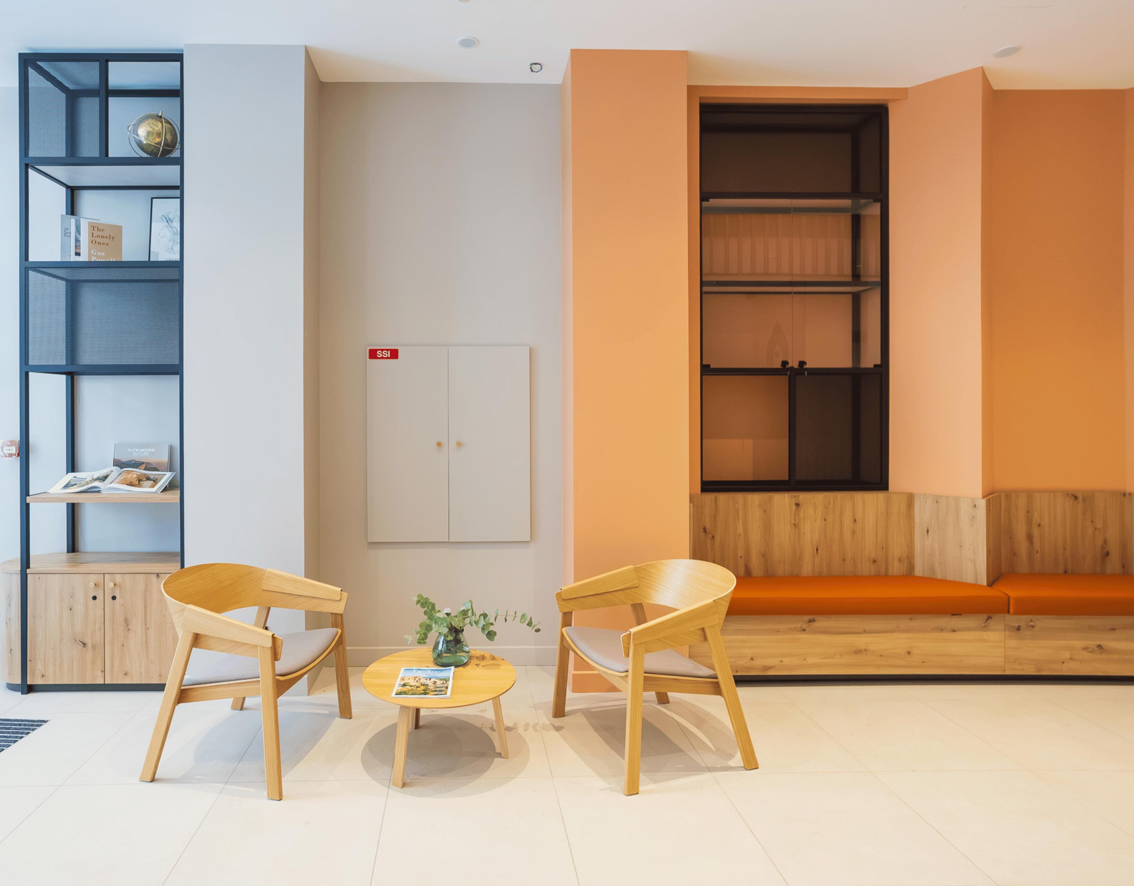 Una habitación moderna con dos sillas de madera, una mesita redonda pequeña, una estantería y un mueble de almacenamiento grande.