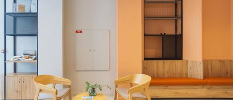 Una habitación moderna con dos sillas de madera, una mesita redonda pequeña, una estantería y un mueble de almacenamiento grande.