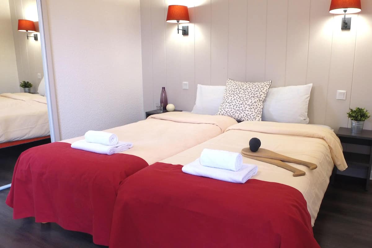 A hotel room with two beds, red and beige bedding, a wooden walking stick, and a small potted plant.